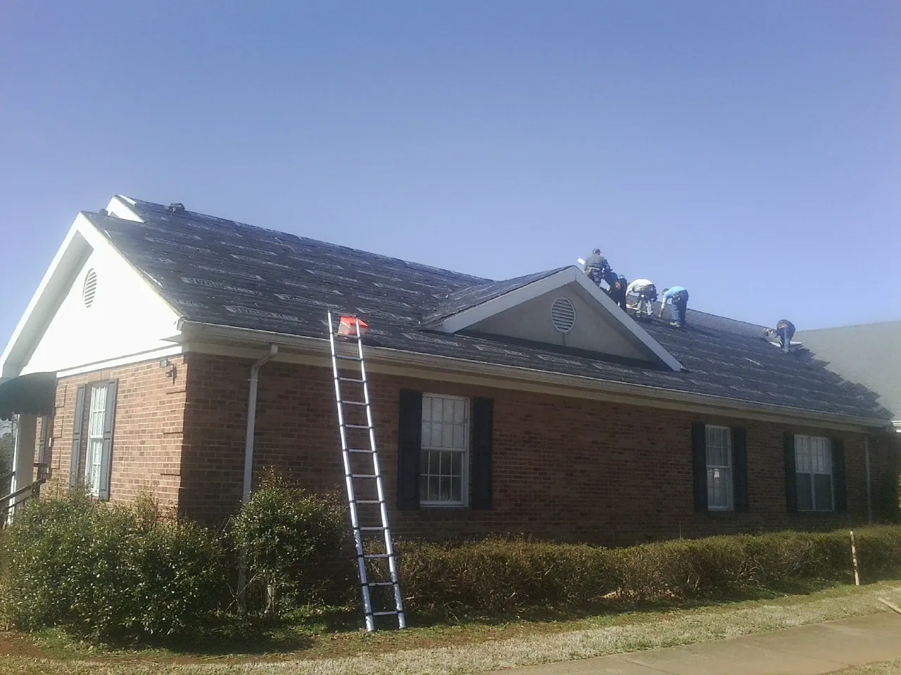 Crew tearing shingles off a brick ranch roof with a ladder set — Emergency Roof Repair work by our crew in Howard